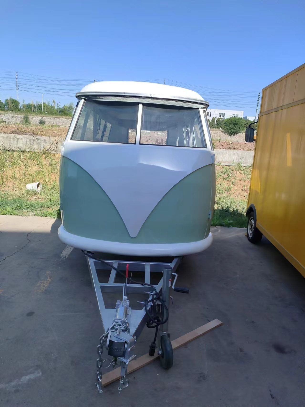 Ein hellgrün-weißes Wohnmobil in Form eines VW-Busses auf einem Anhänger.