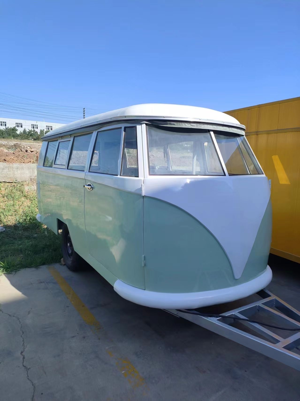 Ein grüner und weißer VW-Bus im Vintage-Stil auf einem Anhänger, der an einem sonnigen Tag draußen parkt.