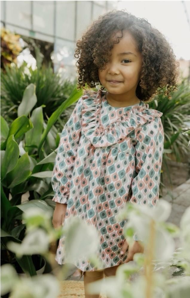 Una chica con un vestido floral sonríe entre exuberantes plantas verdes.