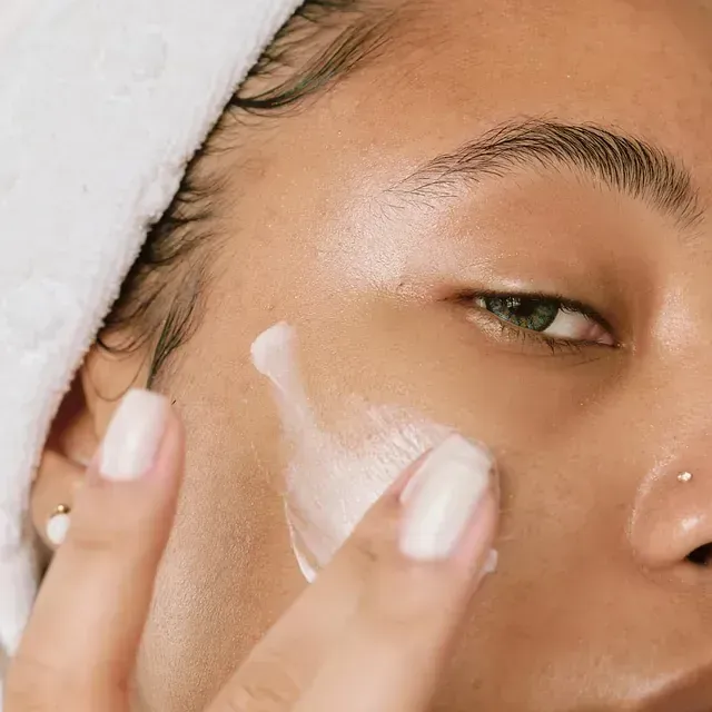 Un primer plano de una mujer aplicándose crema en la cara.