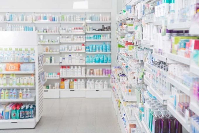 Estanterías repletas de diversos productos farmacéuticos y artículos para el cuidado de la piel en un pasillo de farmacia bien iluminado y organizado.