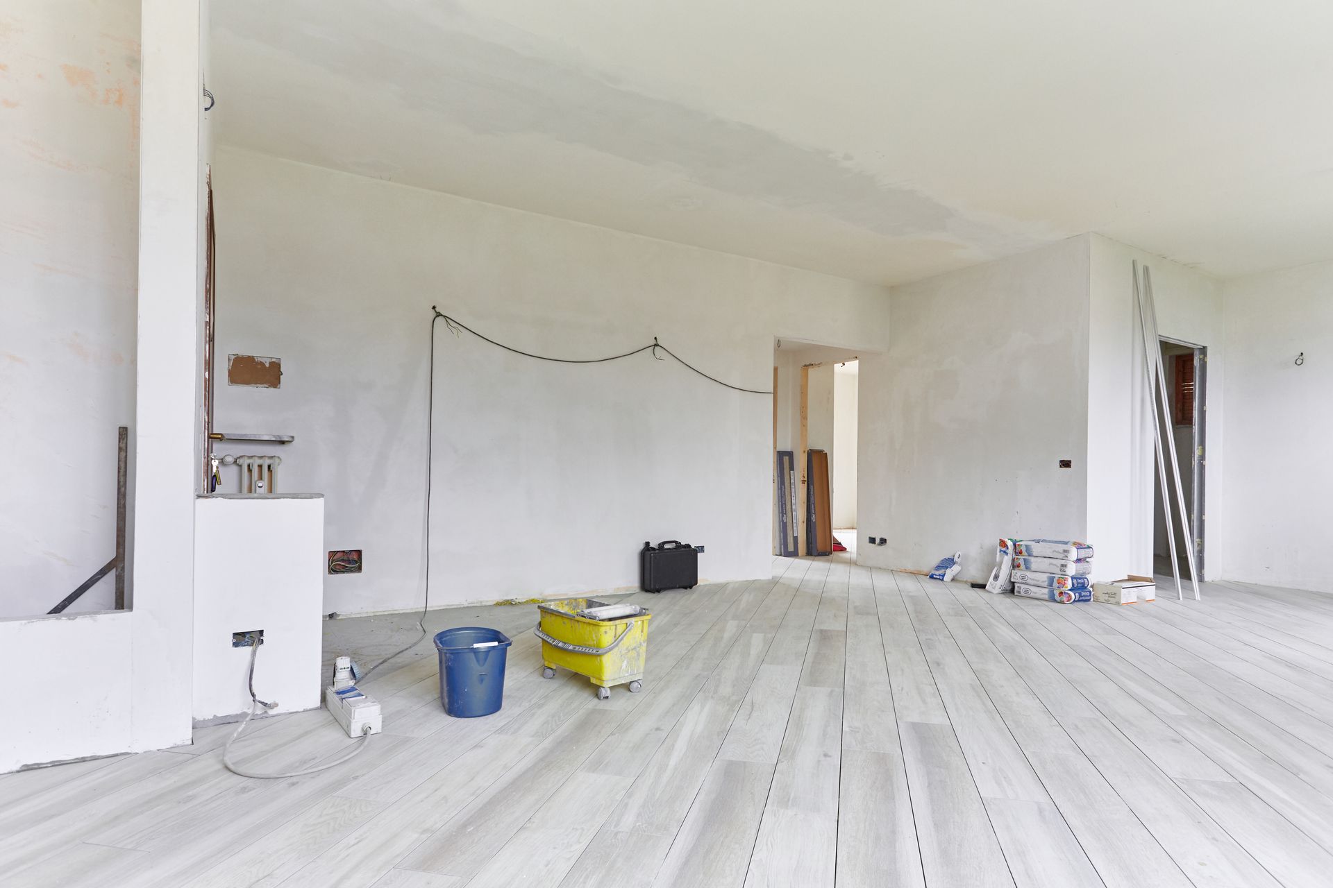 Pièce blanche vide en cours de rénovation avec des seaux de peinture et des outils éparpillés sur le sol.