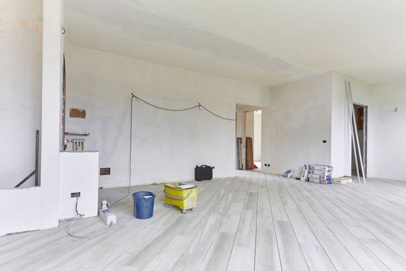 Pièce blanche vide en cours de rénovation avec un parquet, des pots de peinture et des fournitures éparpillés un peu partout.