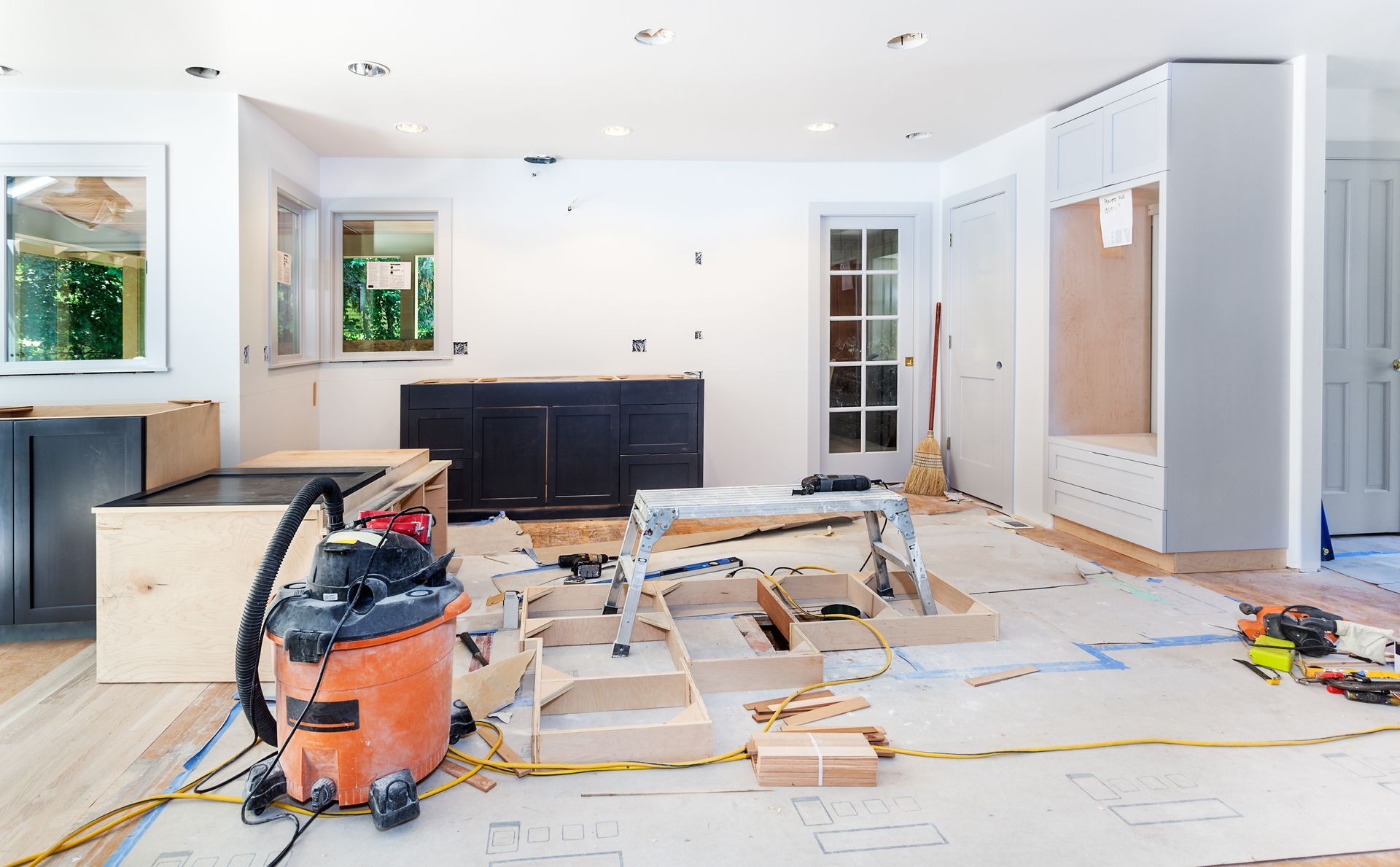 Cuisine lumineuse en cours de rénovation avec des outils éparpillés, des placards et un sol non fini