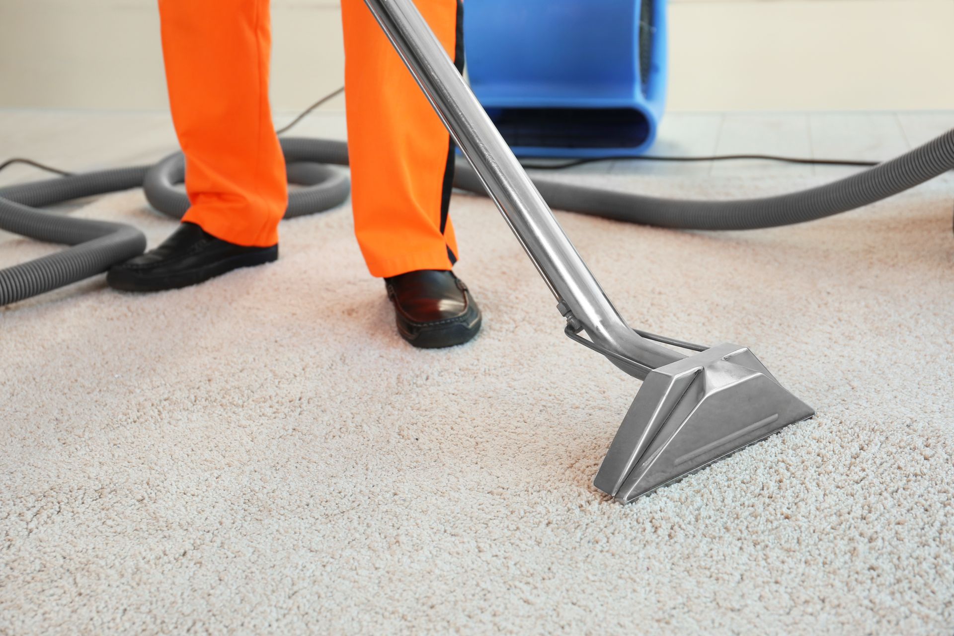 Une tête d'aspirateur pour tapis est posée sur un sol gris clair à côté d'un employé en pantalon orange et chaussures noires.