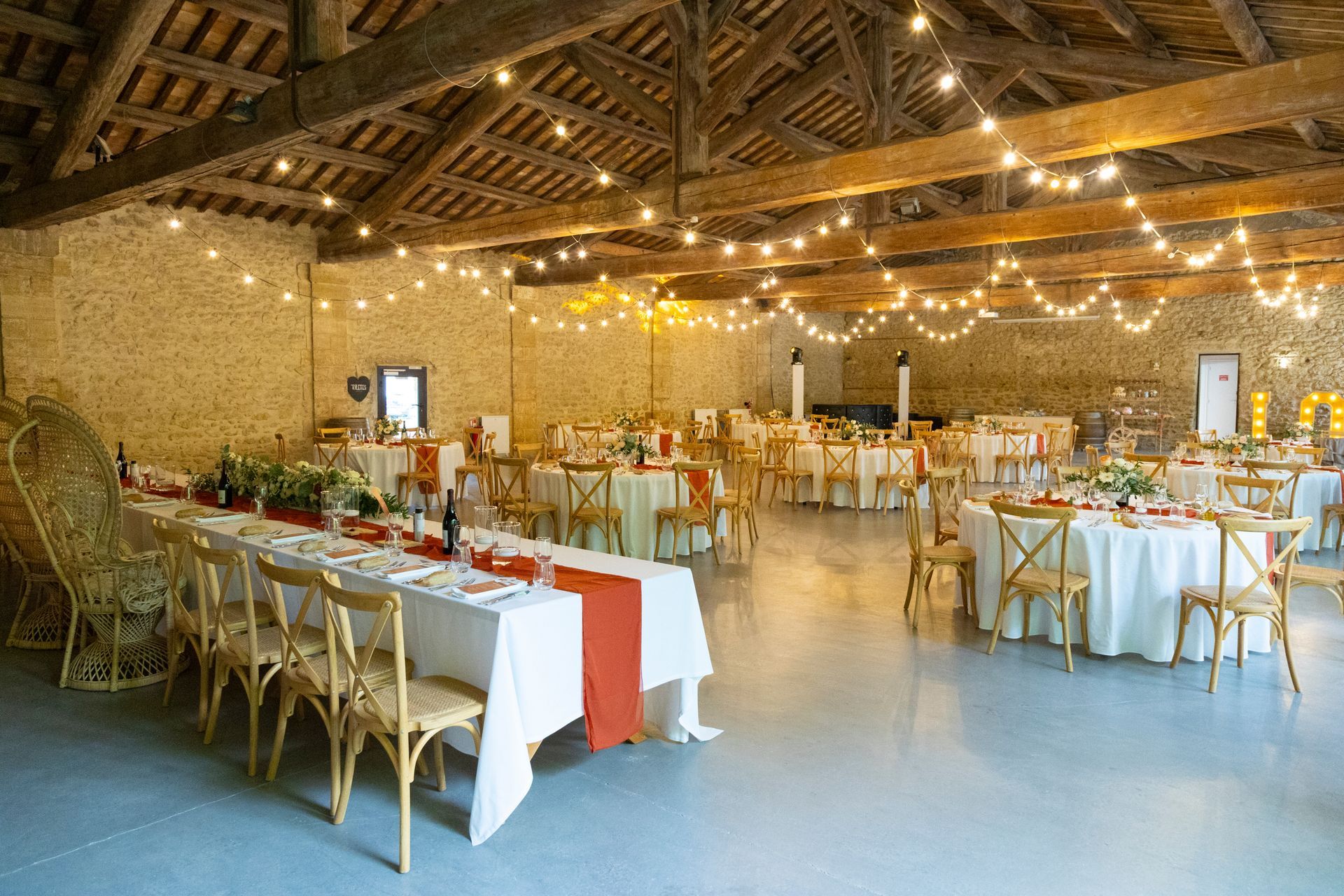 Salle de réception de mariage rustique décorée avec de longues tables blanches, des chaises dorées et des guirlandes lumineuses