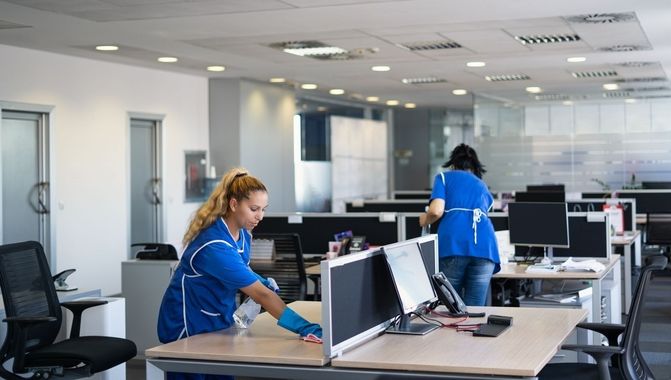 Des agents d'entretien nettoient les bureaux dans un espace de travail ouvert et lumineux.