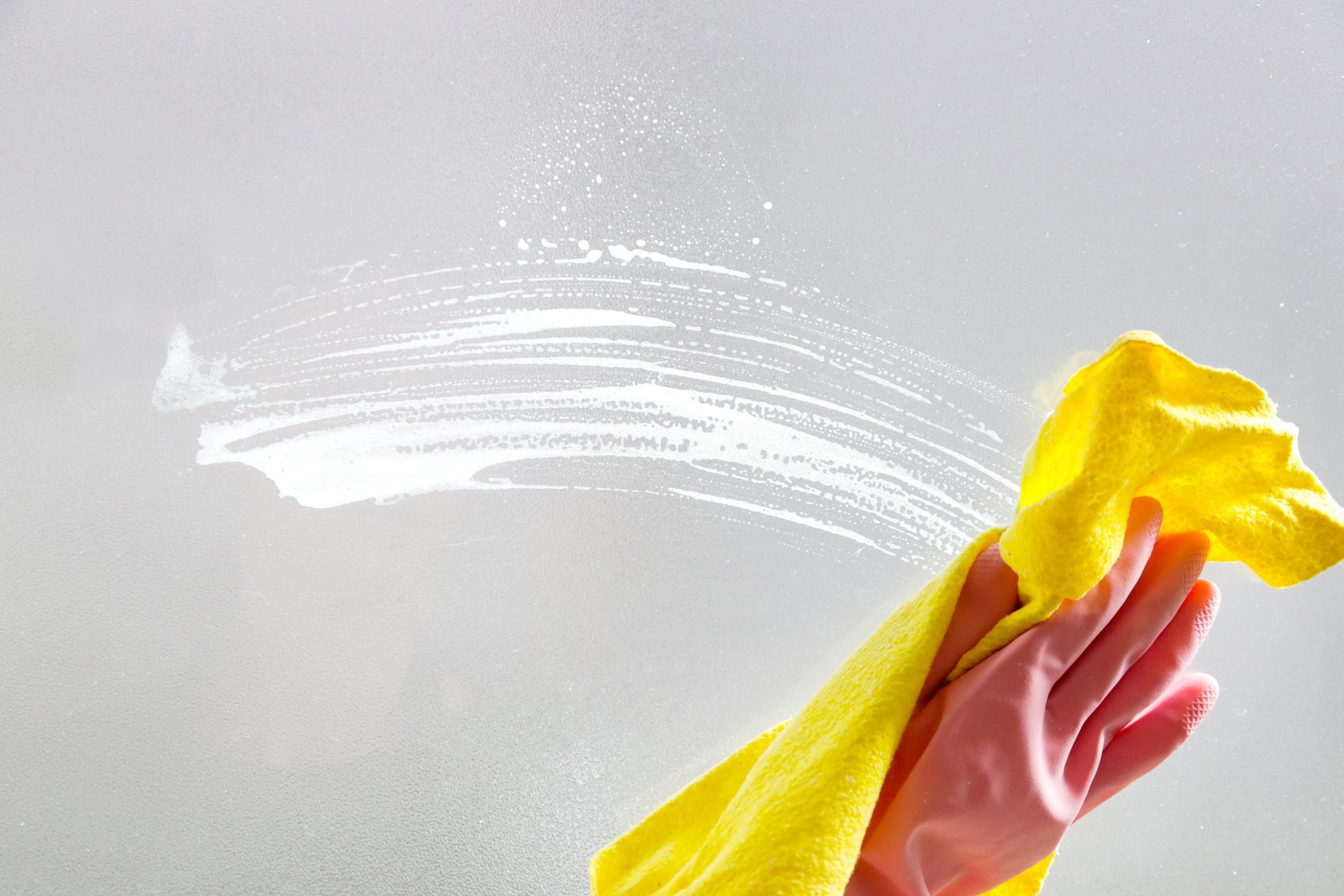 Nettoyage à la main d'une surface blanche avec un chiffon jaune, laissant une trace incurvée de produit nettoyant derrière.
