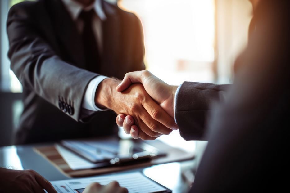 Dos personas de traje se dan la mano en una mesa, con documentos visibles.