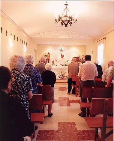 Un grupo de personas está sentado en una iglesia con cruces en la pared.