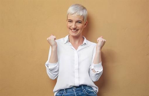 Eine Frau mit kurzen Haaren steht mit ihren Fäusten in der Luft und lächelt.