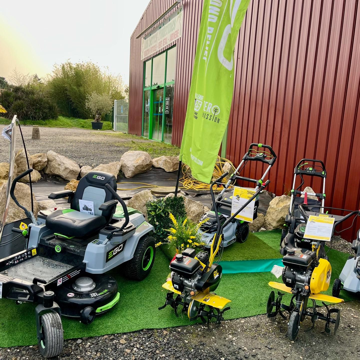 Trois tondeuses à gazon vertes et noires exposées à l'extérieur, près d'un bâtiment et de rochers.