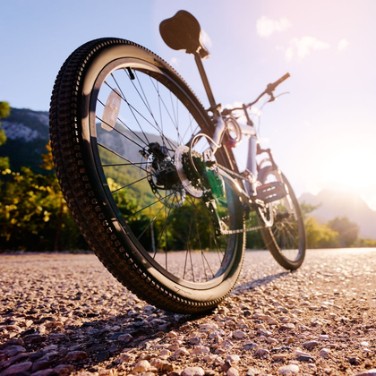 VTT sur un chemin de gravier ensoleillé, vu d'un angle bas avec des montagnes en arrière-plan.