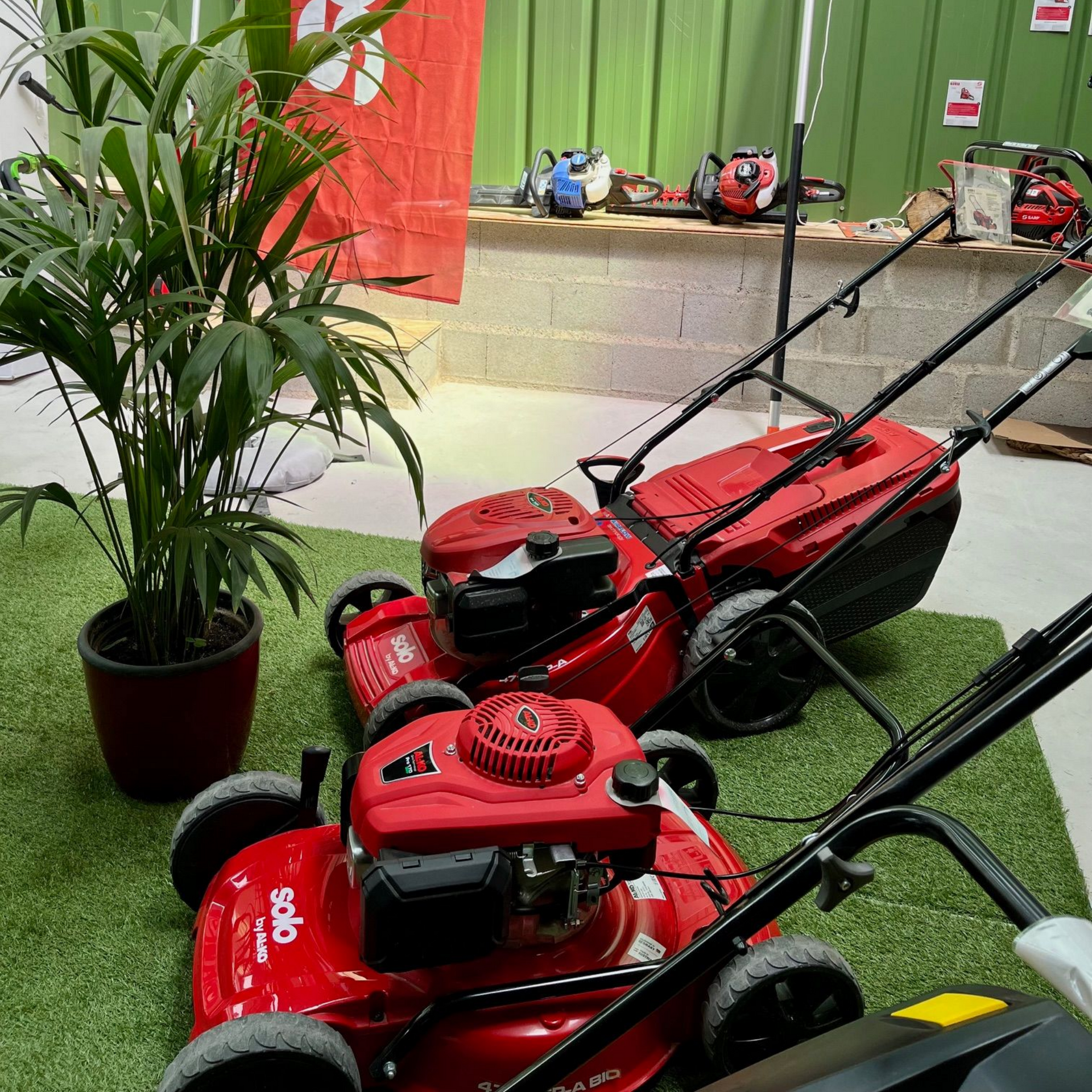 Des tondeuses à gazon rouges exposées sur du gazon artificiel lors d'un salon du matériel de jardinage.