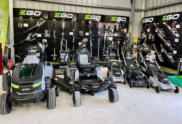 Présentoir EGO avec plusieurs tondeuses à gazon électriques et outils de jardin alignés à l'intérieur.