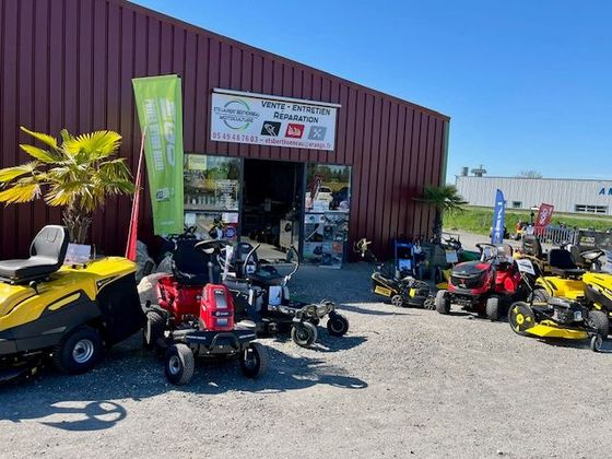 Magasin de sports motorisés de plein air avec des quads, des motos tout-terrain et un kart rouge garé devant un bâtiment bordeaux.