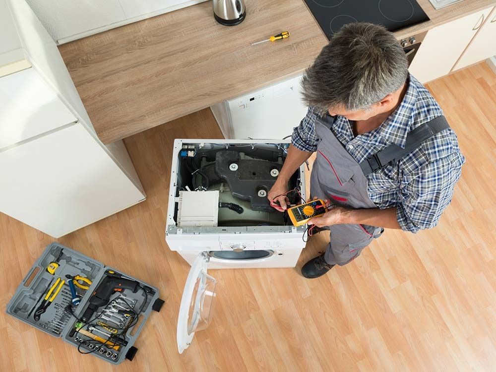 Un hombre está arreglando una lavadora en una cocina.