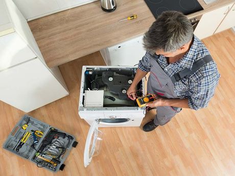 Un hombre está arreglando una lavadora en una cocina.