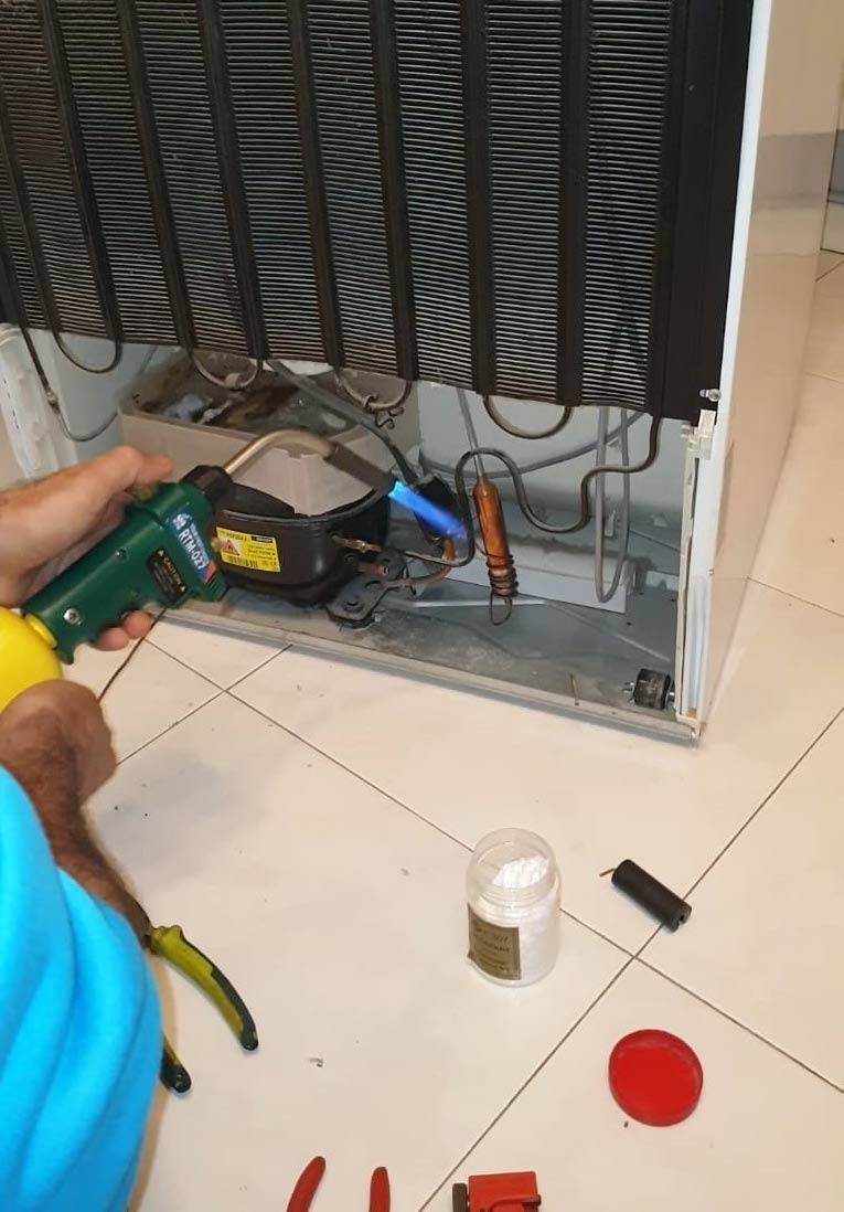Una persona está arreglando un refrigerador con un destornillador.