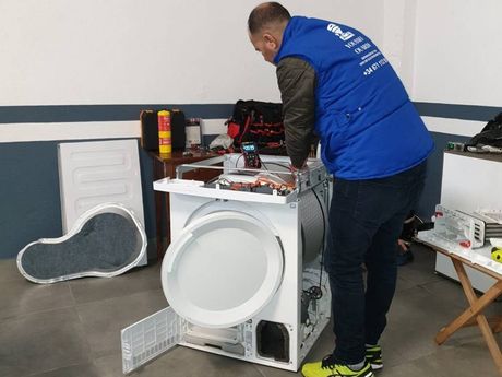 Un hombre con un chaleco azul está trabajando en una lavadora.