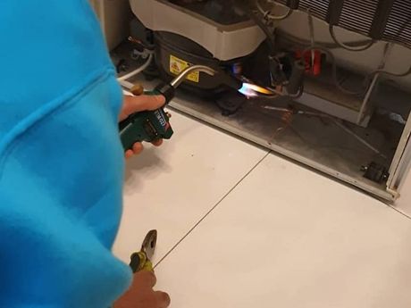 Una persona está usando un soplete para arreglar un refrigerador.