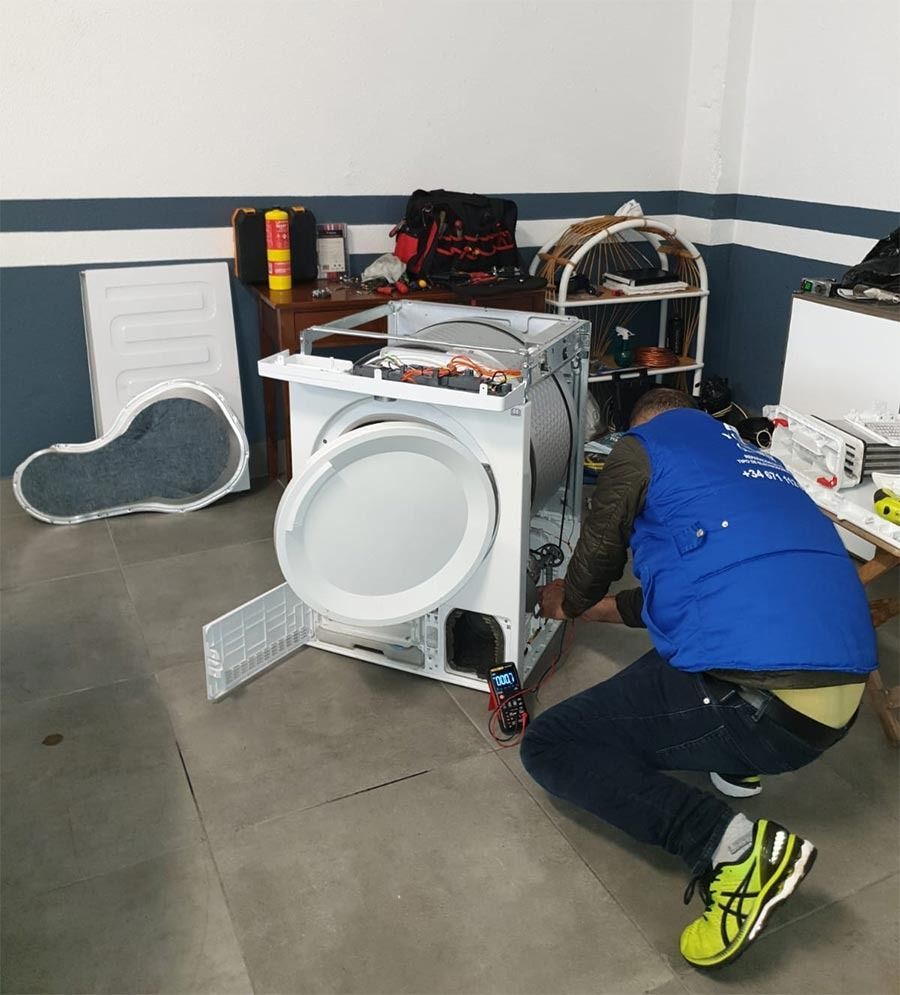 Un hombre con un chaleco azul está trabajando en una lavadora.