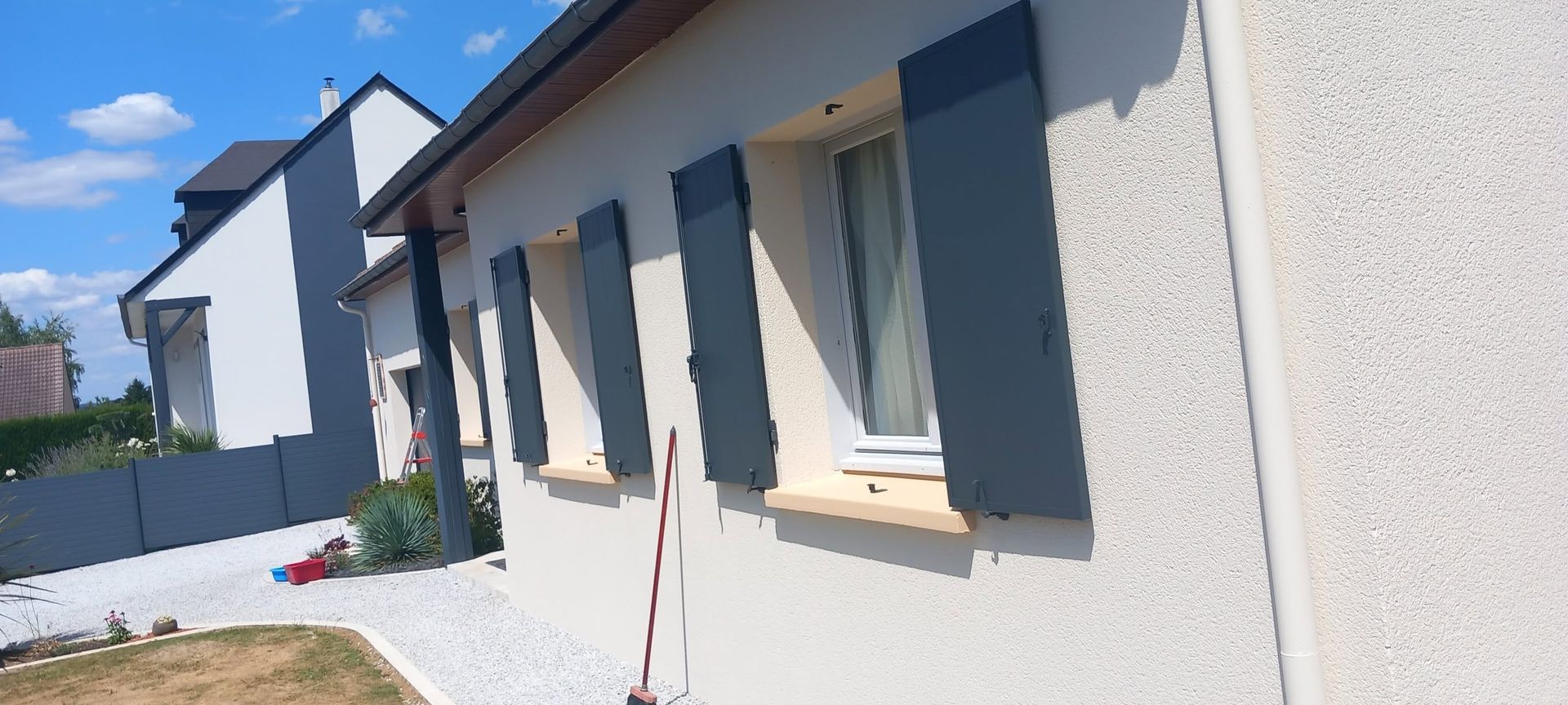 La façade d'une maison blanche aux volets gris.