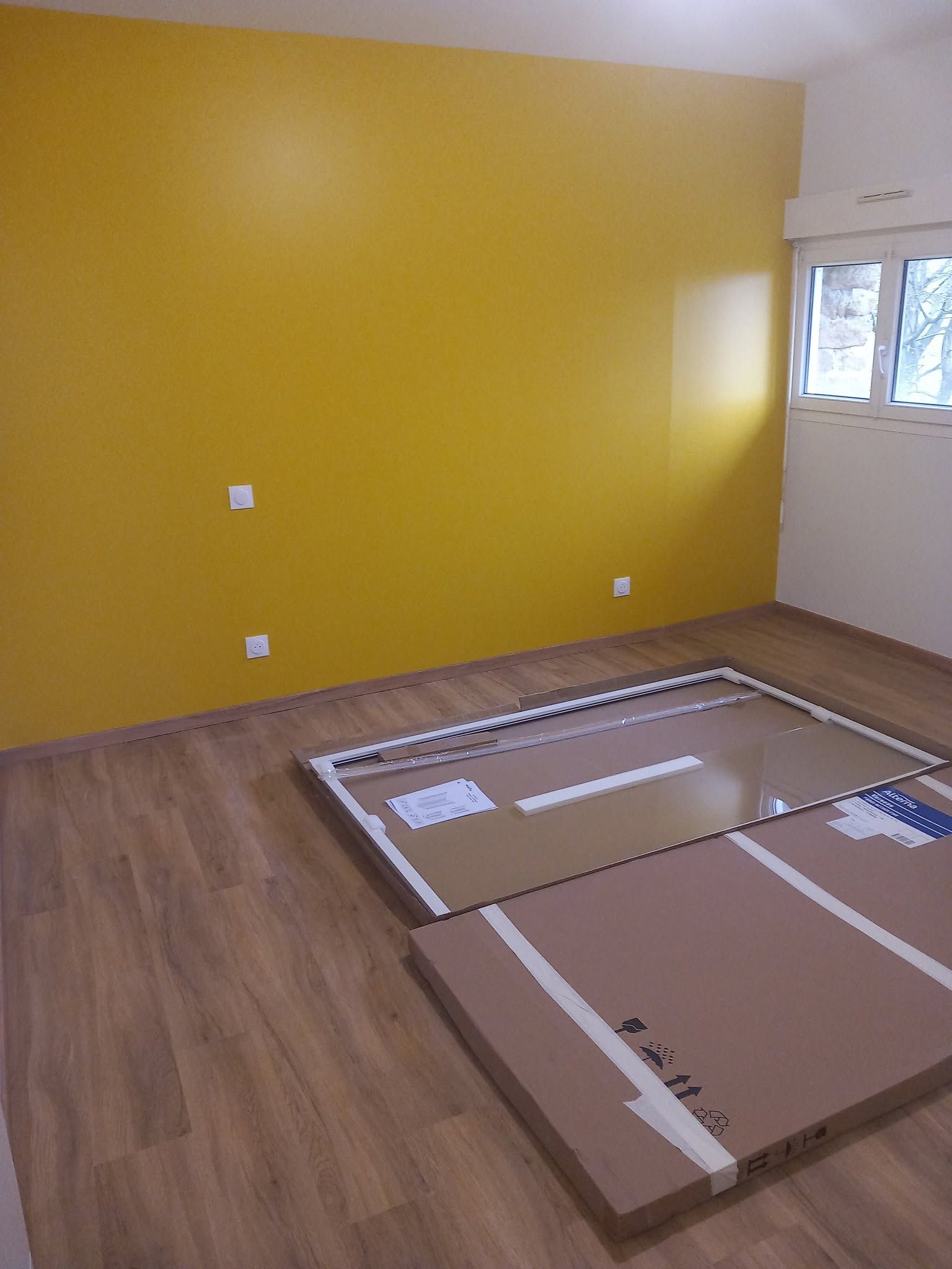 Une pièce vide avec un mur jaune moutarde.