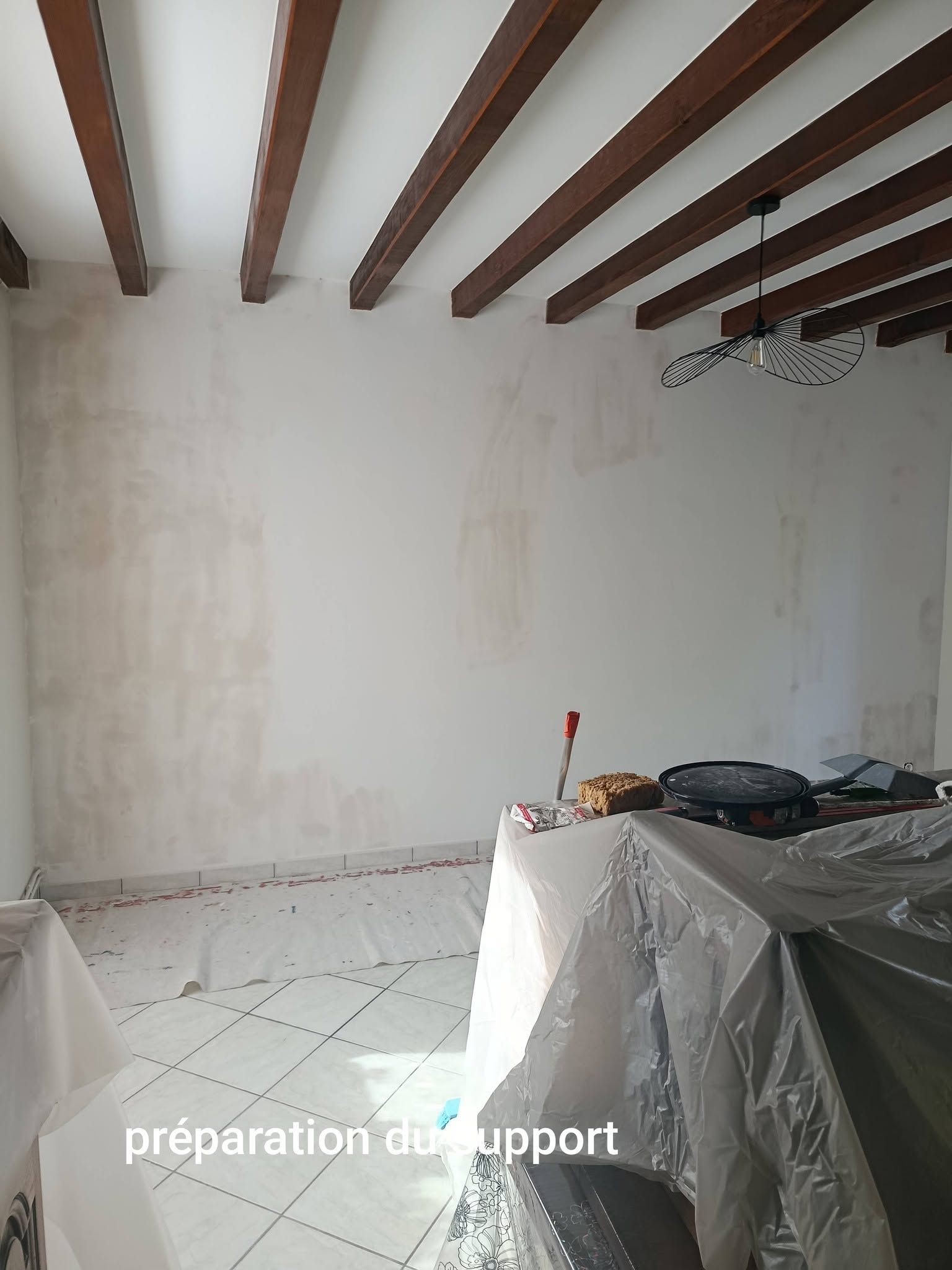 Un mur à rénover, avec des poutres apparentes visibles au plafond.