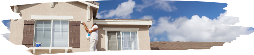 Une personne peint l'extérieur d'une maison sous un ciel bleu.