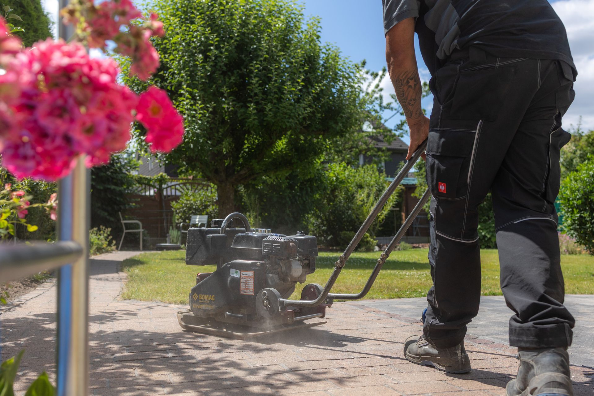 Ein Gärtner bedient an einem sonnigen Tag auf einer Terrasse eine Rüttelplatte