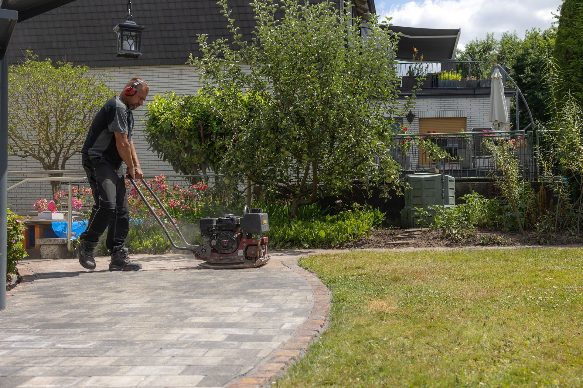 Ein Arbeiter verdichtet Pflastersteine ​​mit einer Vibrationsplatte in einem Hinterhofgarten