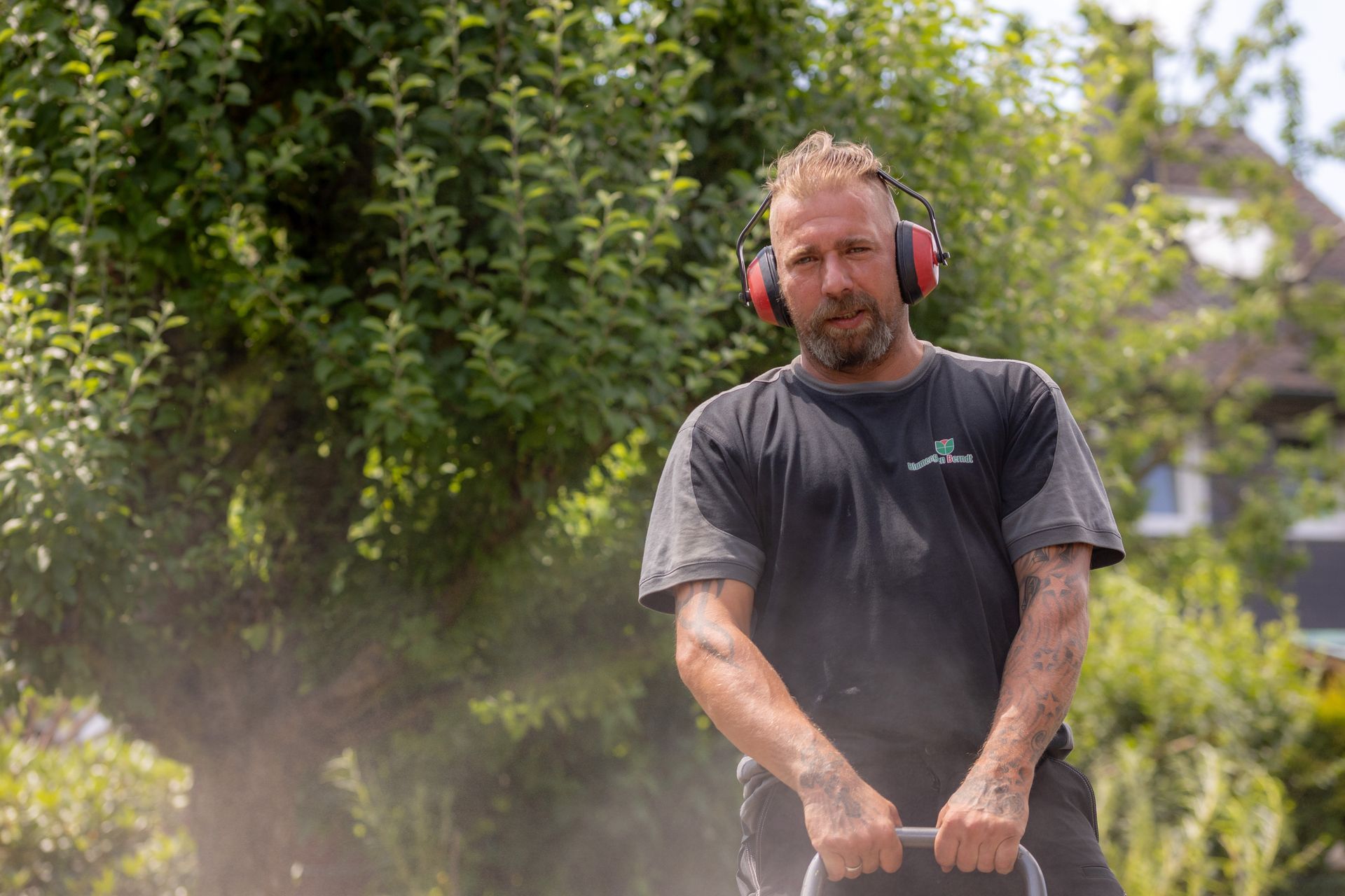 Ein Gärtner mit Gehörschutz bedient im Freien eine Rüttelplatte, die den Terrassenboden festigt