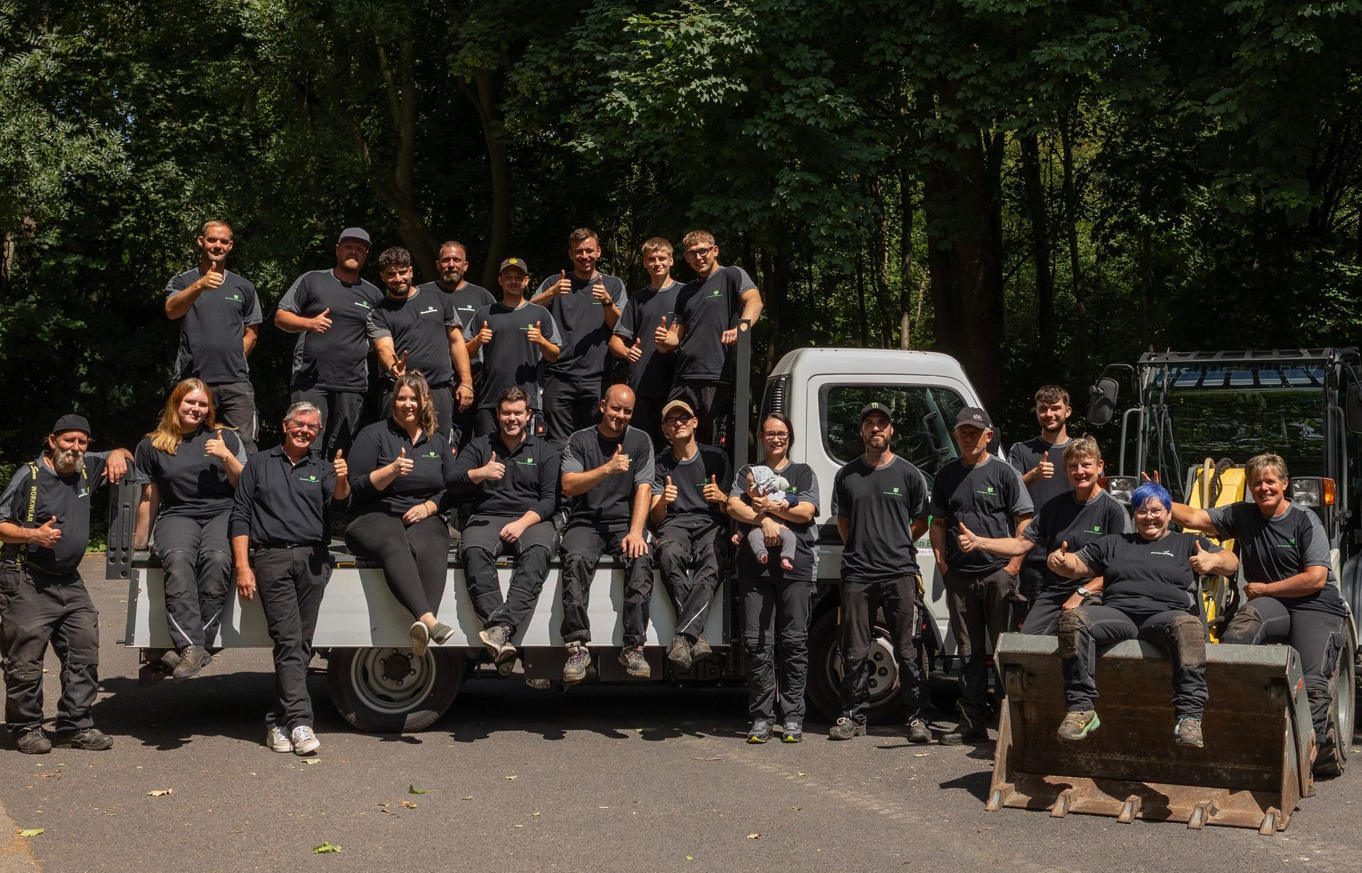 Ein Teamfoto der Blumengarten Berndt KG vor und auf ihren Fahrzeugen in einem Waldgebiet.