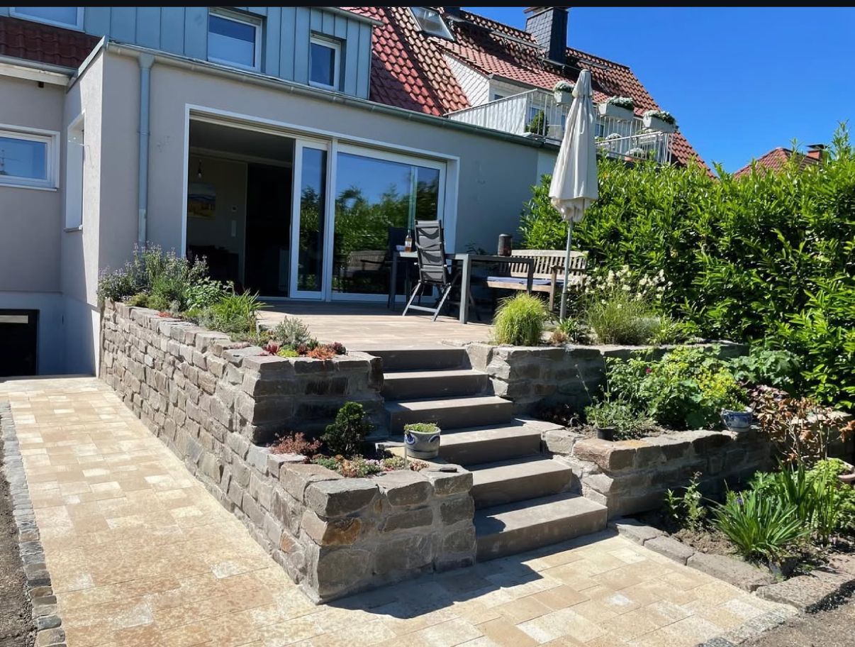 Steinstufen einer Terrasse führen zu einem Garten, der mit Pflanzen und Sträuchern gestaltet ist