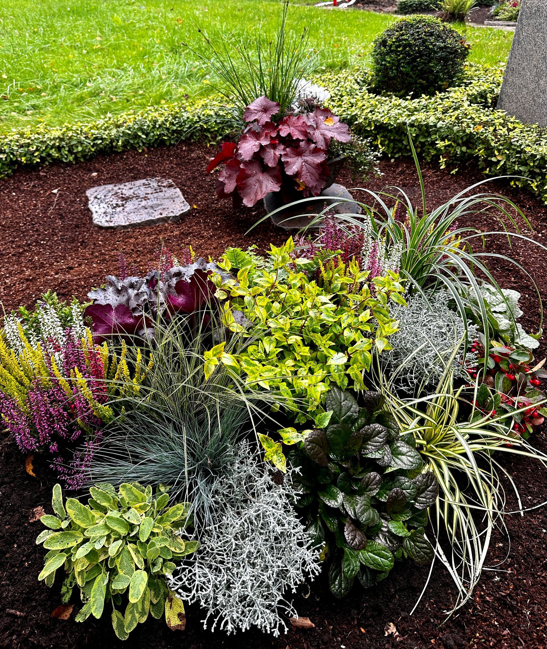 Friedhof mit Steindenkmälern, bunten Blumen und gepflegten Bäumen