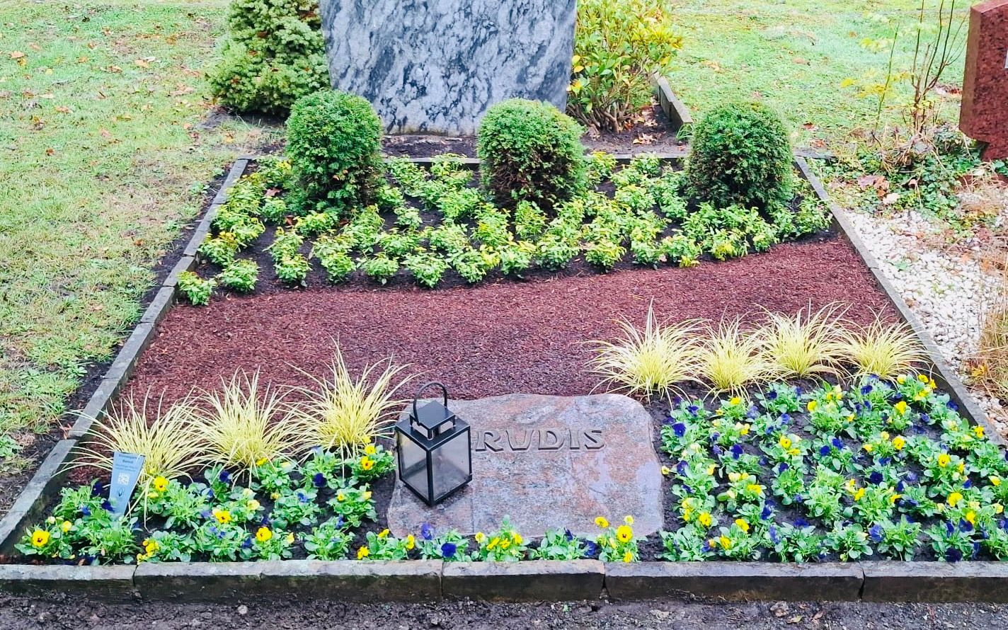 Gepflegtes Grab mit Steinmarkierung, Pflanzen, Kiesweg und Laterne