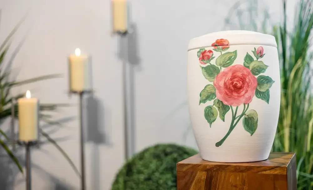 Eine weiße Vase mit einer rosa Rose darauf steht auf einem Holzblock.