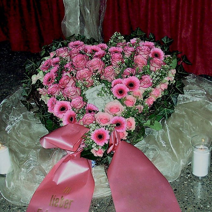 Ein herzförmiger Strauß rosa Blumen mit einer rosa Schleife mit der Aufschrift „Lieber