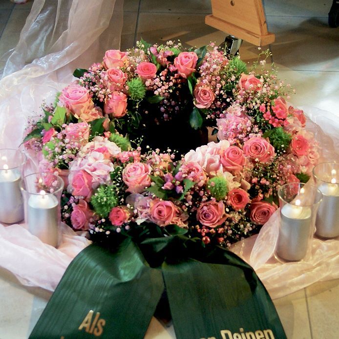 Ein Kranz aus rosa Blumen mit einem grünen Band, auf dem als steht