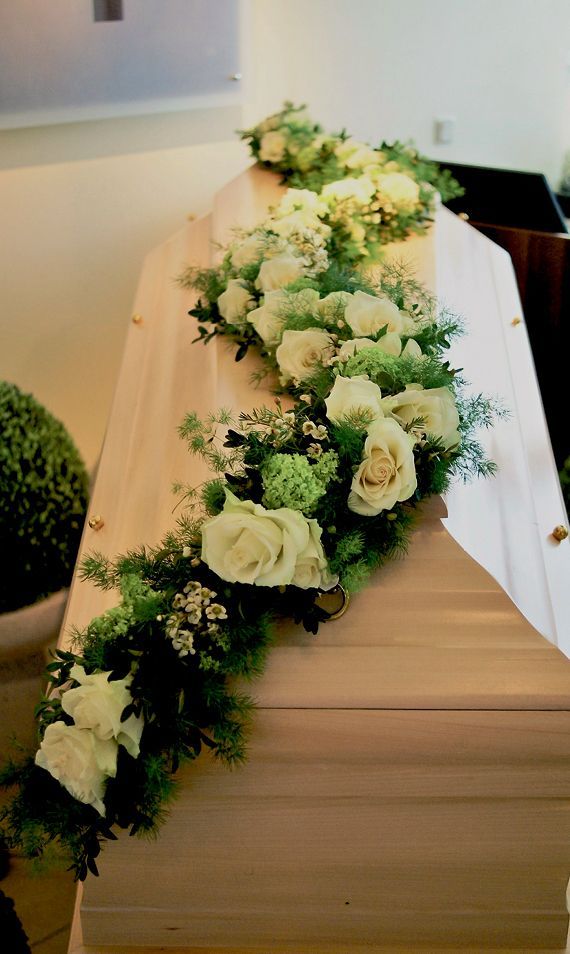 Ein Sarg ist mit weißen Rosen und Grünpflanzen geschmückt.