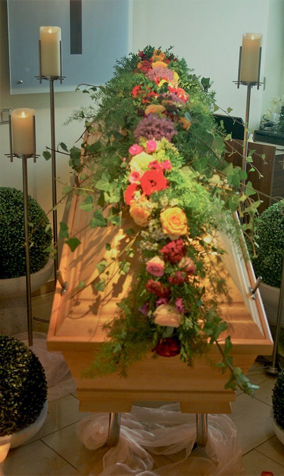 In einem Raum ist ein Sarg mit Blumen und Kerzen geschmückt.