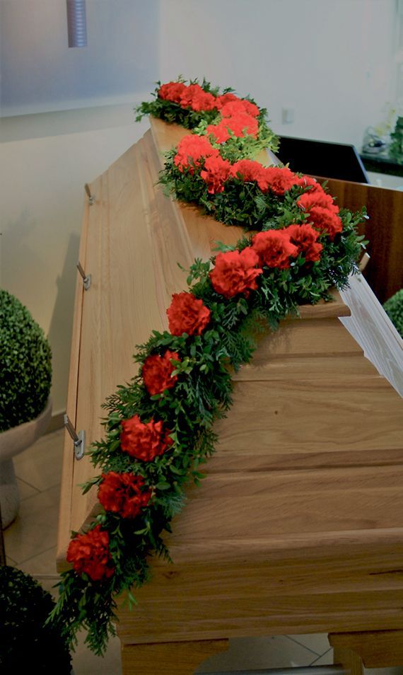 Ein Holzsarg, der mit roten Blumen und Grünpflanzen geschmückt ist.