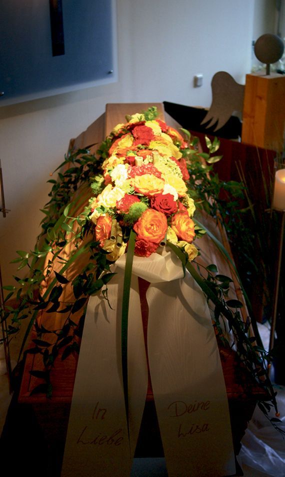 Ein Sarg ist mit Blumen und einem weißen Band geschmückt.