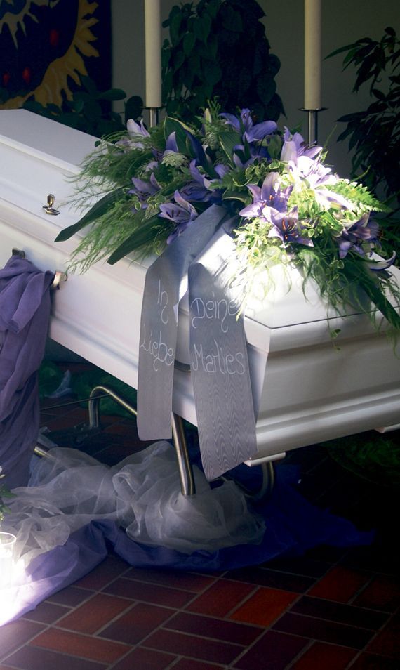 Ein weißer Sarg mit lila Blumen und Kerzen darauf