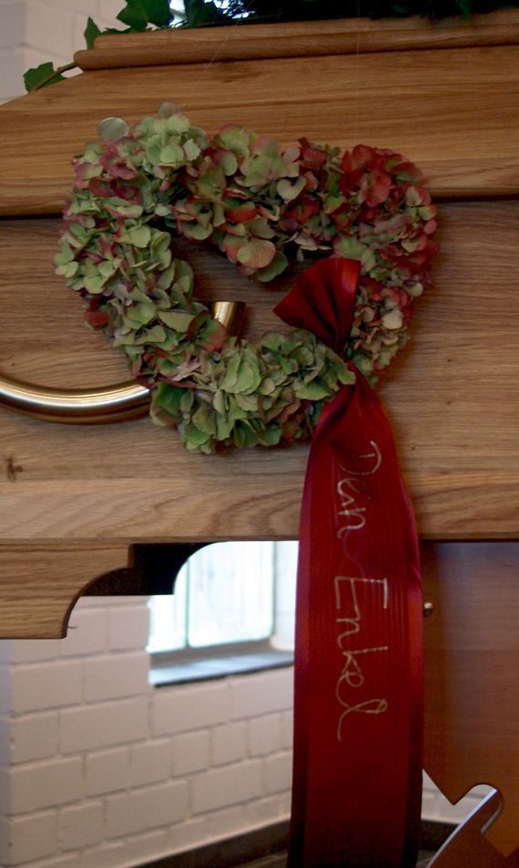 Auf einem Holzsarg liegt ein herzförmiger Kranz.