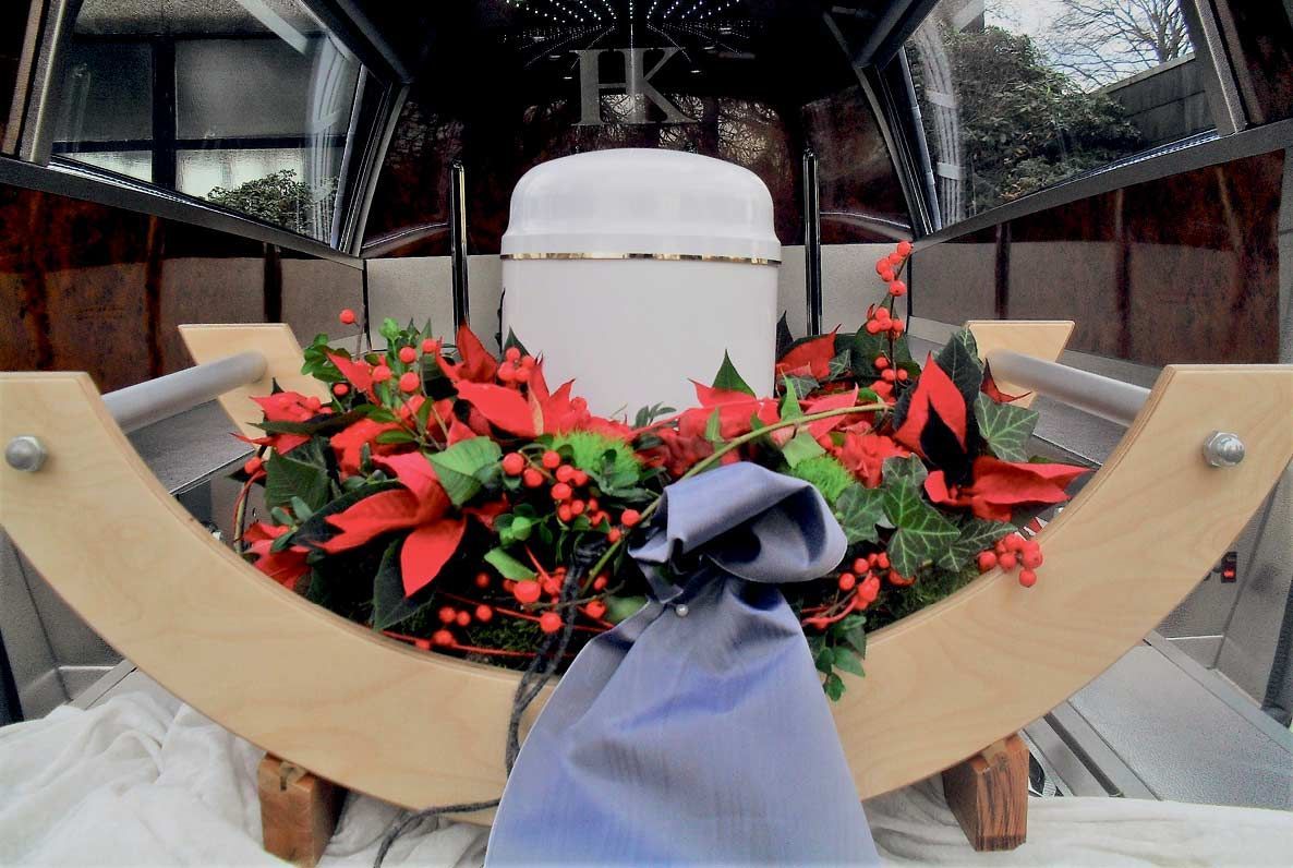 Eine weiße Urne ist von roten Blumen und einem blauen Band umgeben