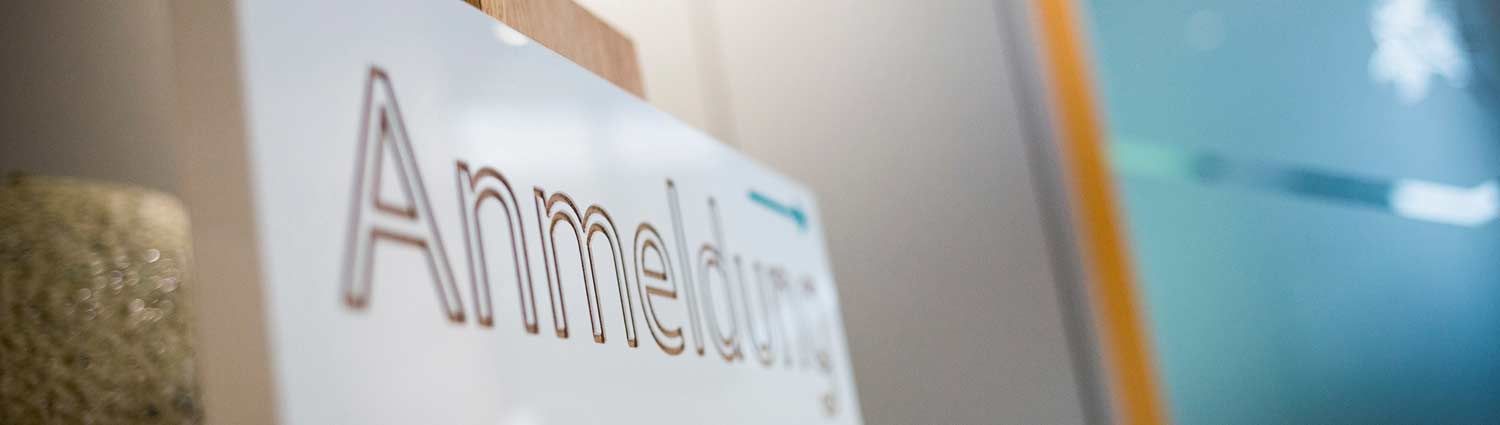 An einer Wand hängt ein weißes Schild mit der Aufschrift „Anmeldung“.