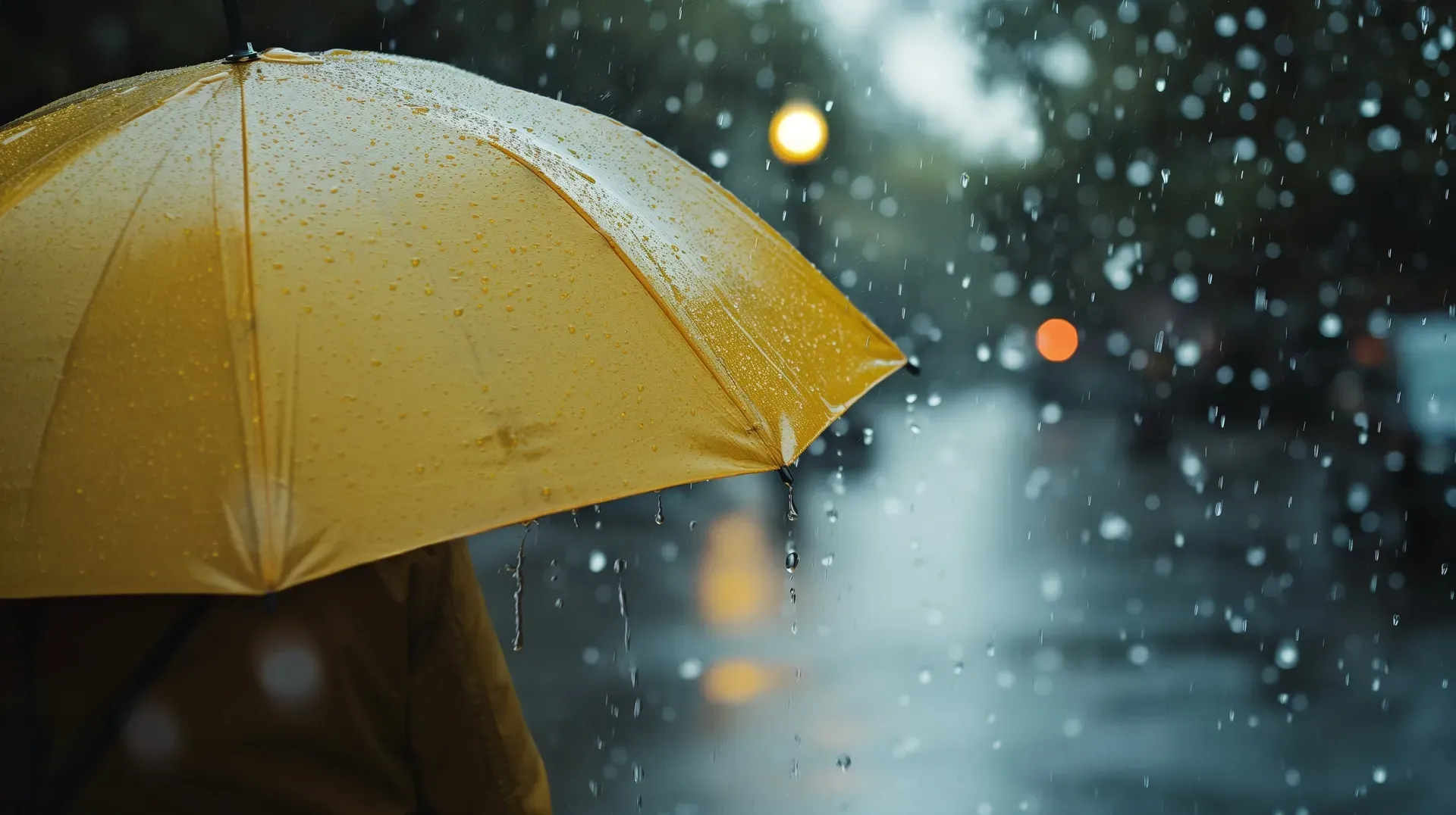 Eine Person hält einen gelben Regenschirm im Regen.