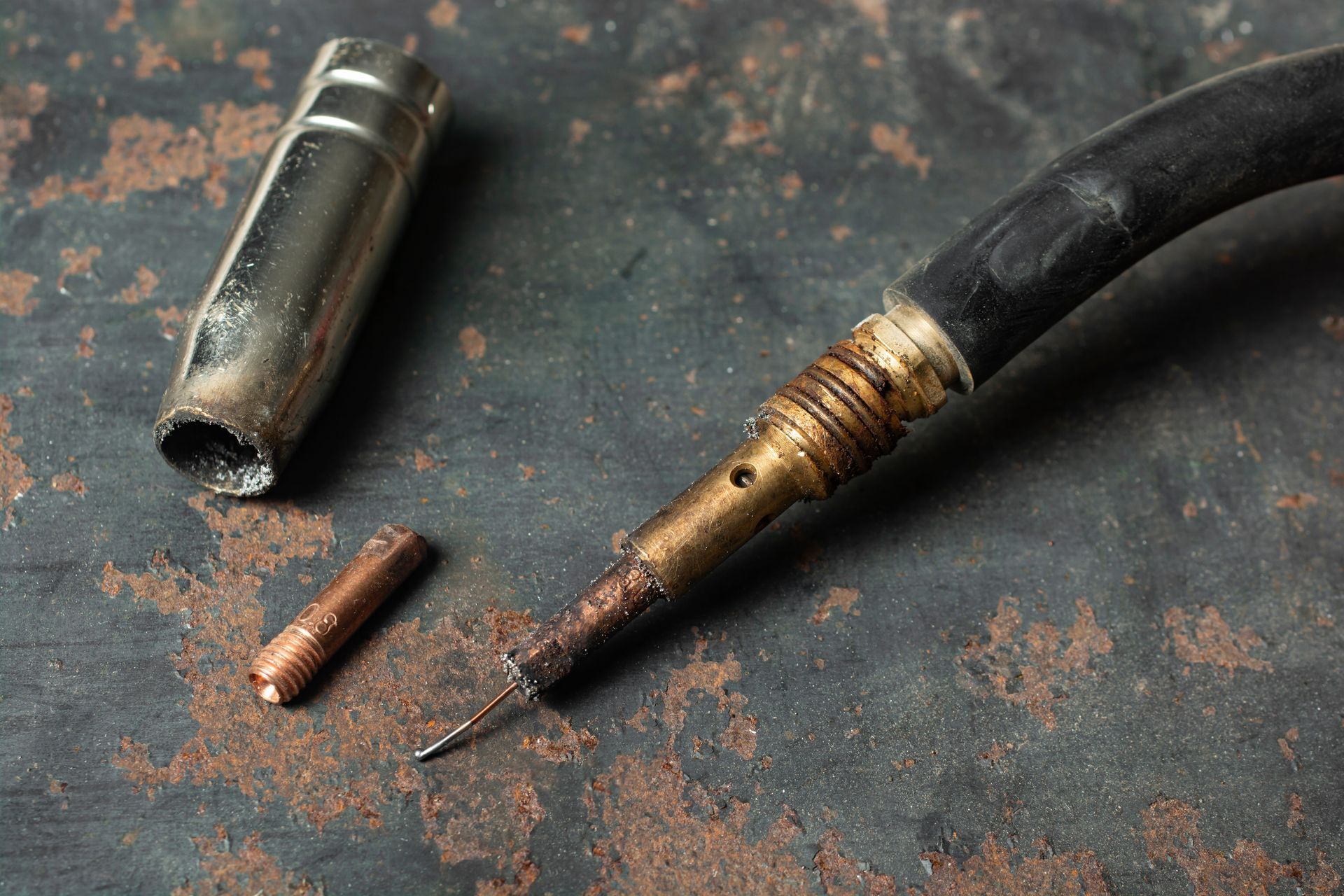 Kaputter Schweißbrenner mit Düse, Spitze und Draht auf einer rostigen Metalloberfläche.